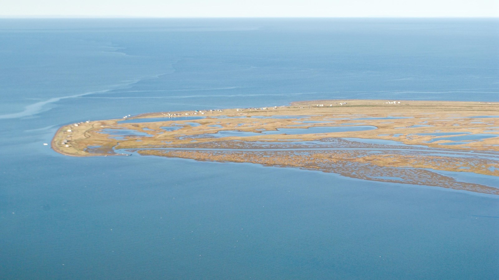 Aerial view of coastal fishing village with small white tents and multiple lakes