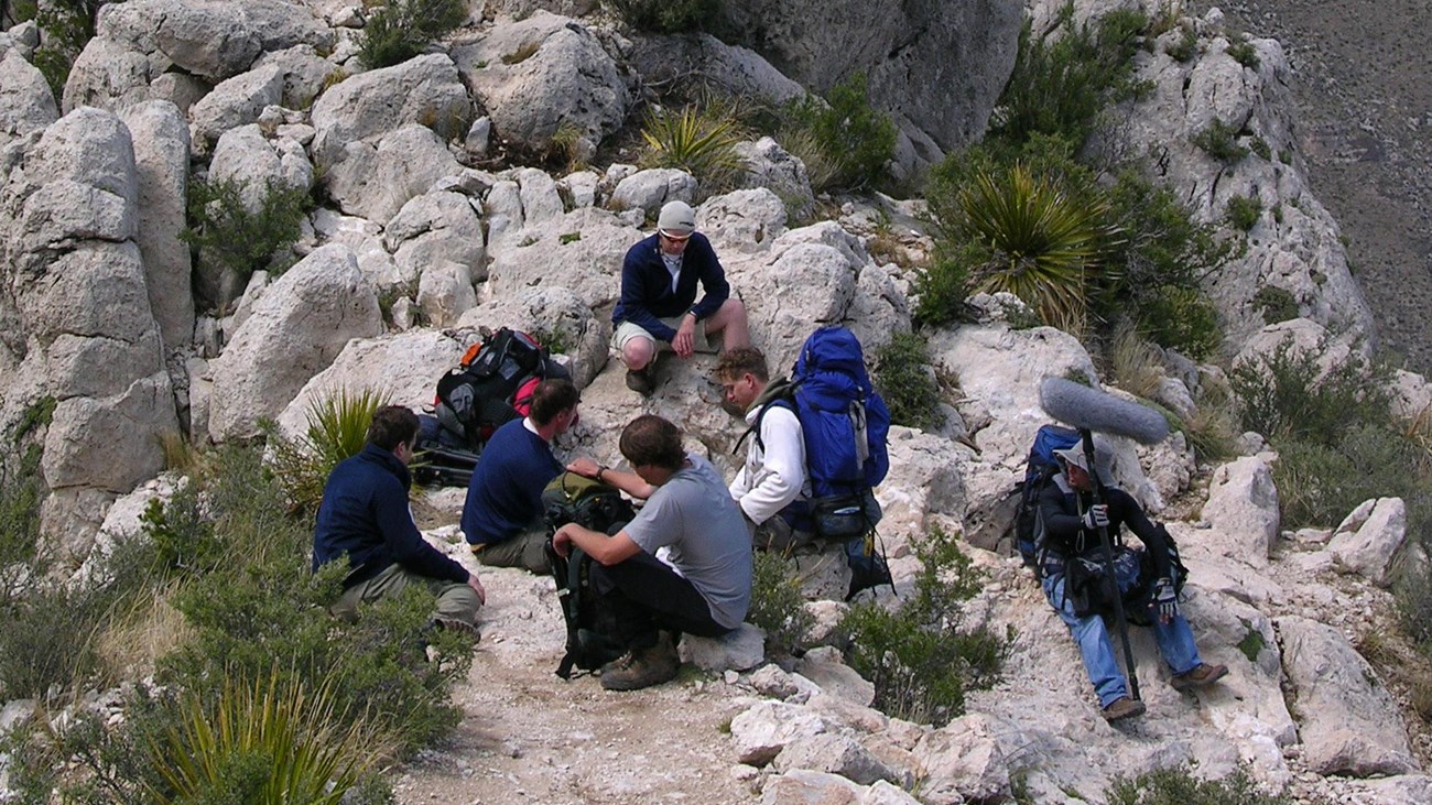 A group of hikers relax along a trail high up on a mountain