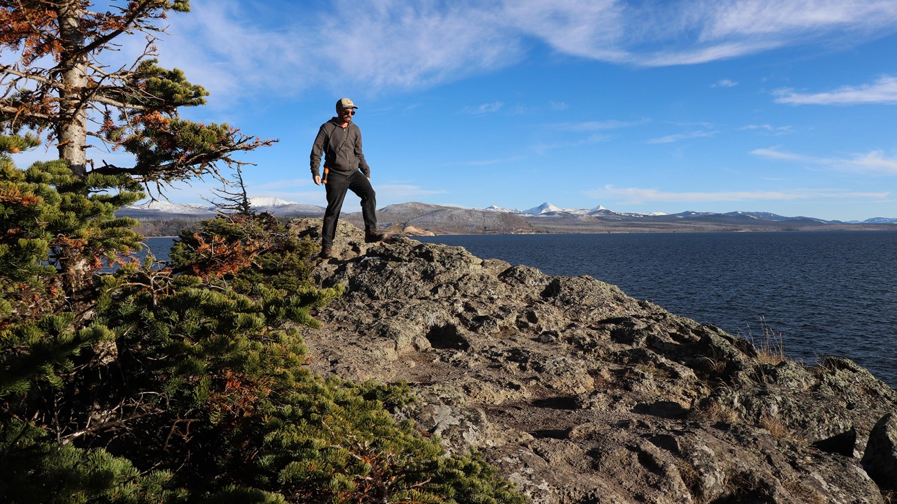 A hiker walks across a rocky outcropping above a large lake.