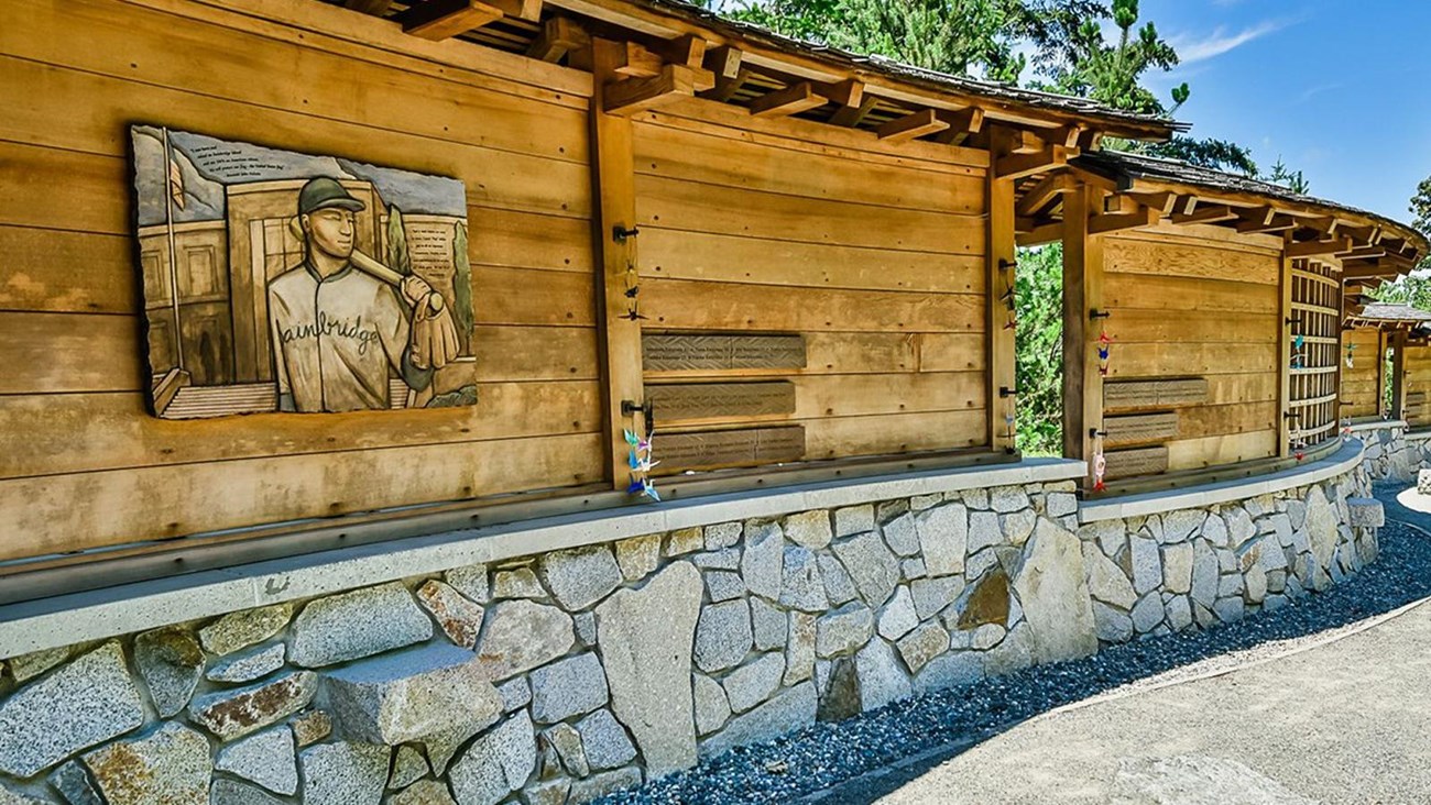 Wooden panels above stone wall along a paved walkway.
