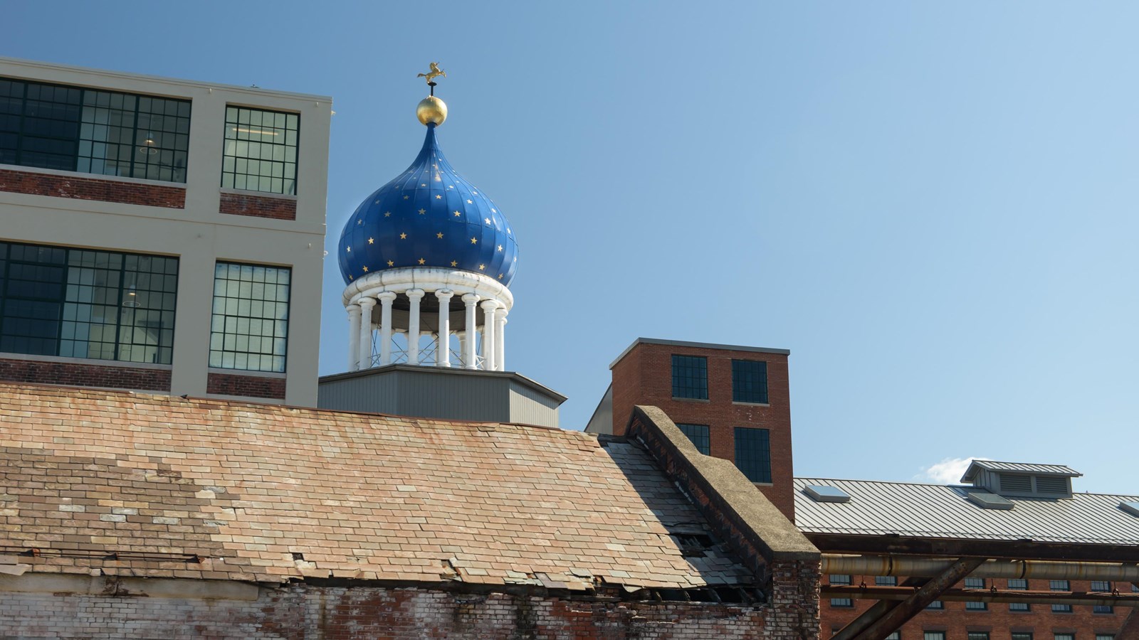 A blue onion dome behind a brownstone building and next to a white building on a clear day.