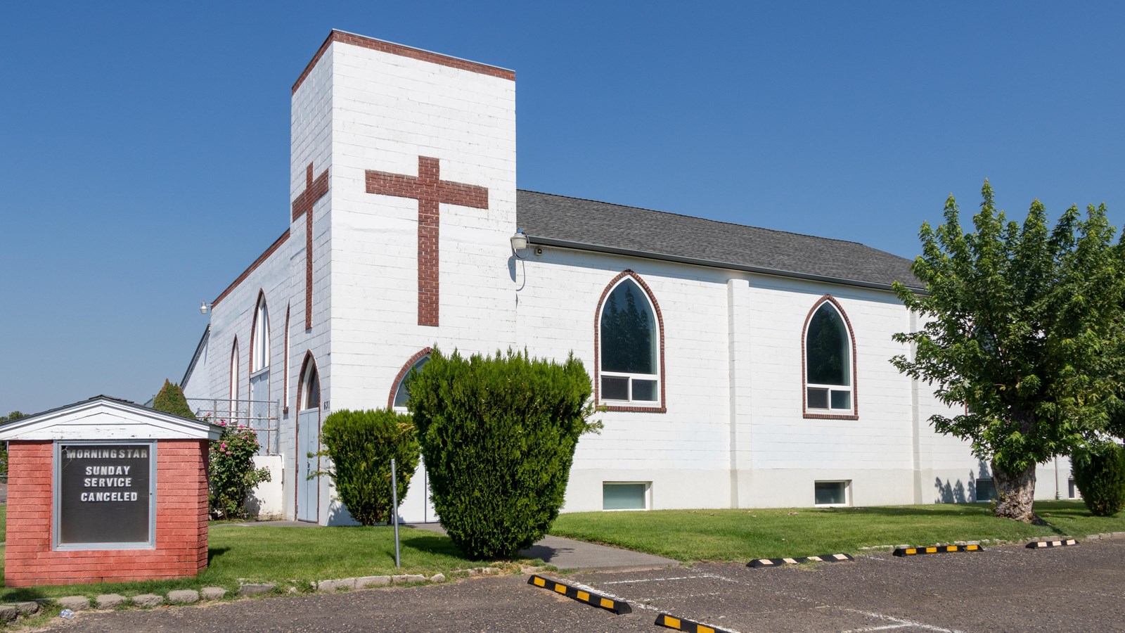 Color photograph of a white brick church. The church has 10 oval windows.