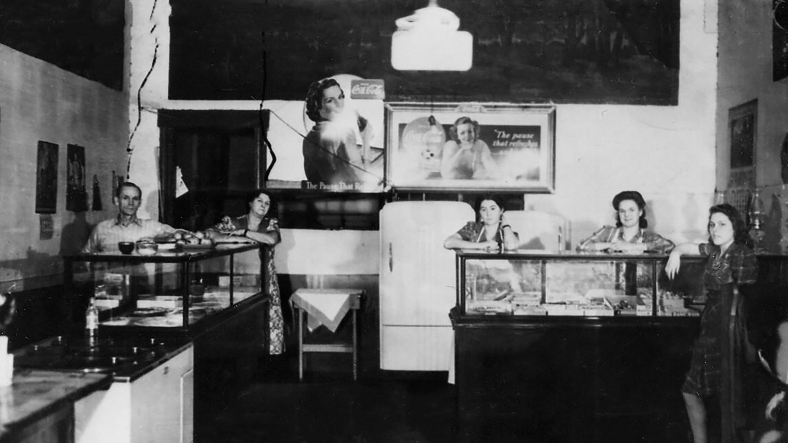 The inside of a restaurant with counters and tables and chairs. Smiling people lean on the counter.