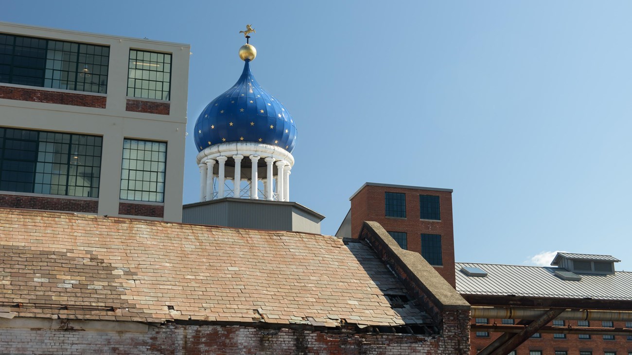 A blue onion dome behind a brownstone building and next to a white building on a clear day.