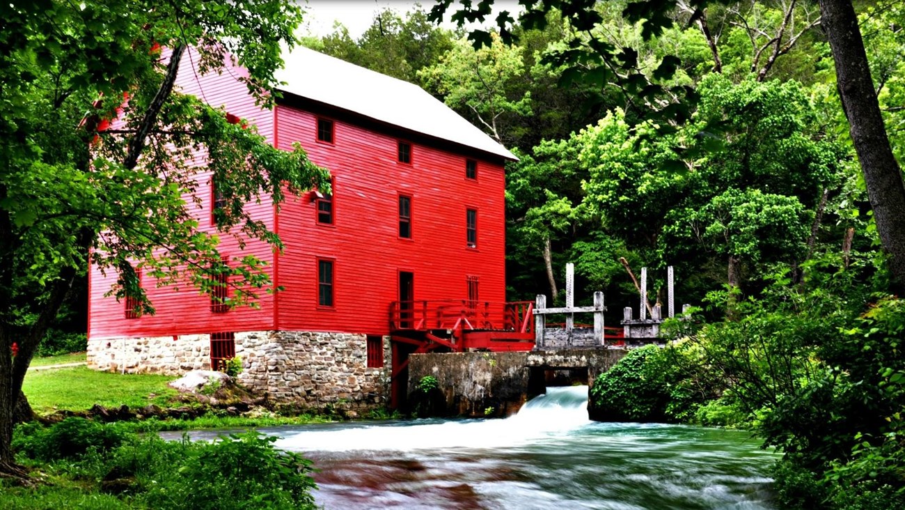 Alley Mill painted in red up close with Alley Spring flowing clear and blue from it.