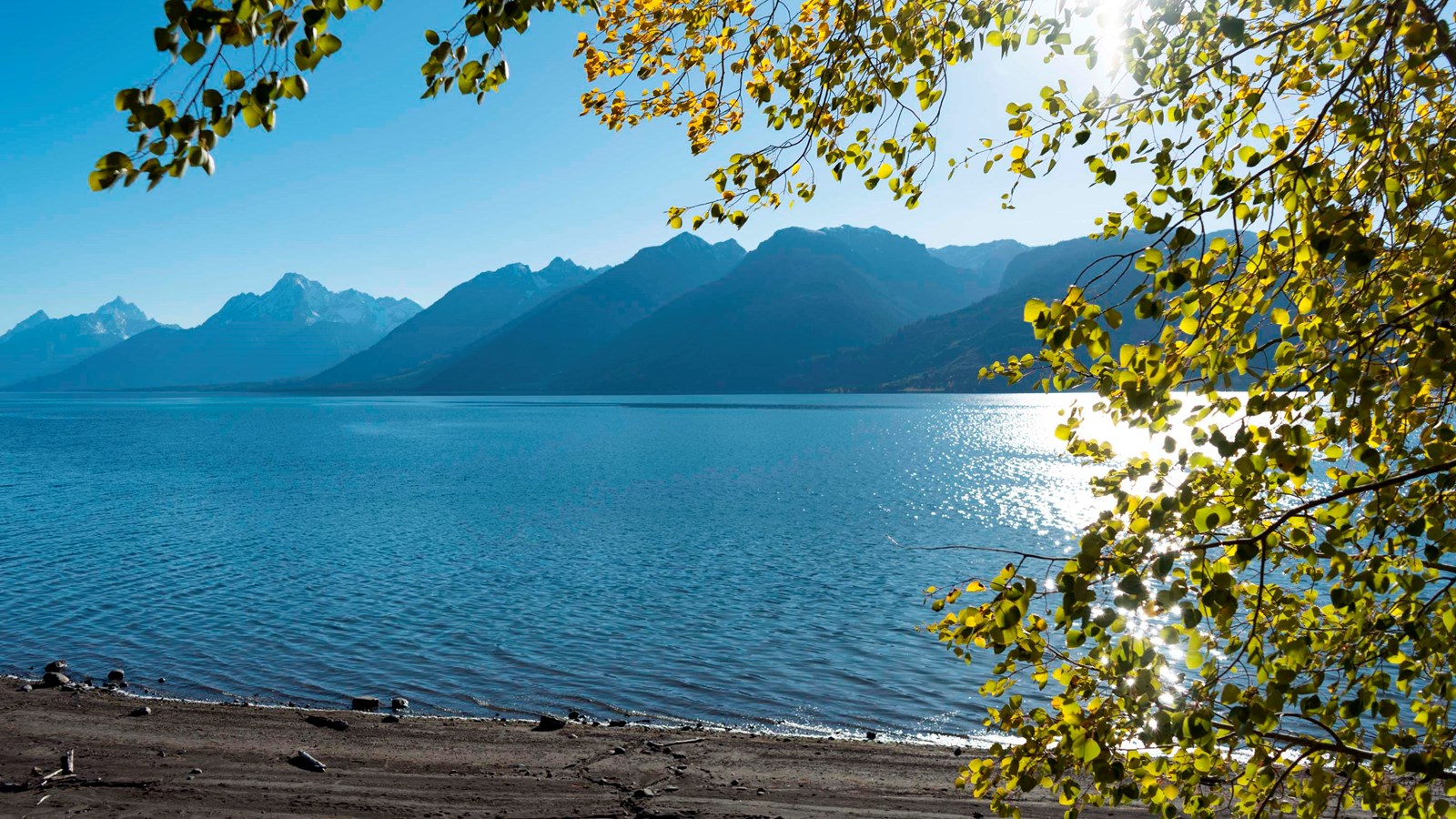 A beach and lake with mountains and a blue sky in the background