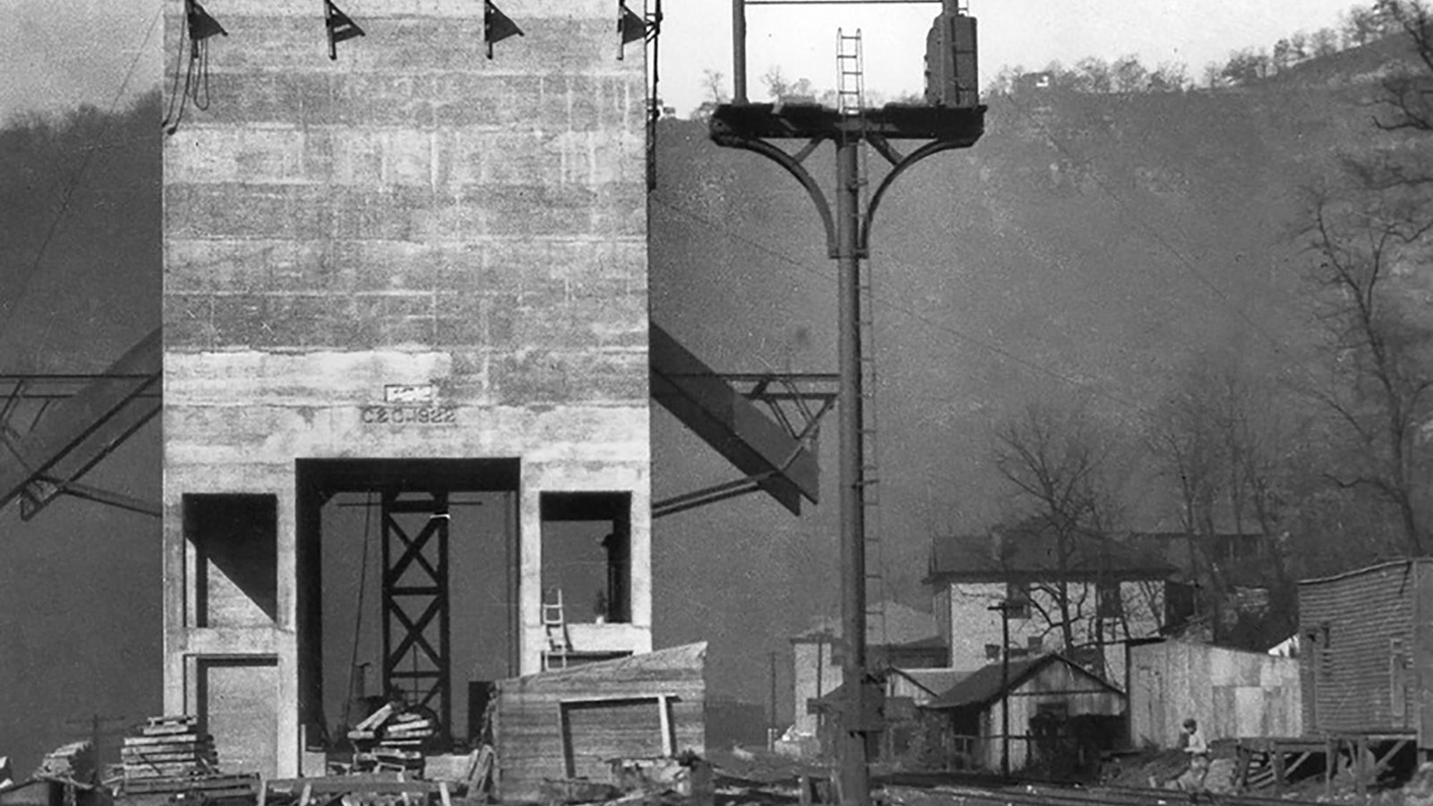 A tall square cement tower on thick cement legs with metal shoots coming out towards railroad tracks