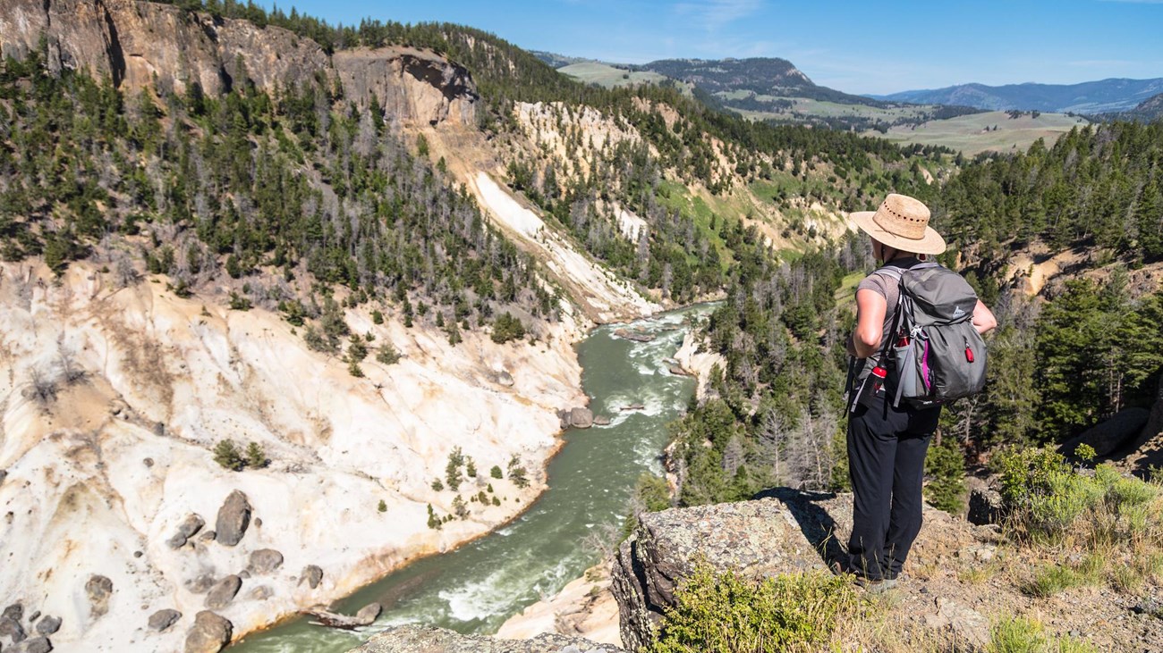 A hiker stands on the edge of a canyon and looks down at the river below.