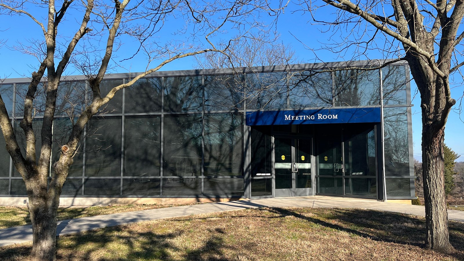 A paved walkway leads to a glass building and a set of double doors.