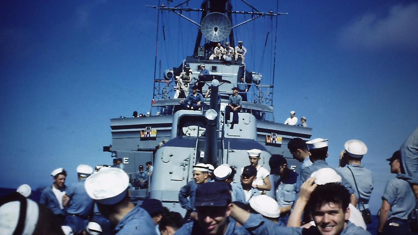 Men in sailor\'s dungarees sit on a ship deck and on gun turrets in background.