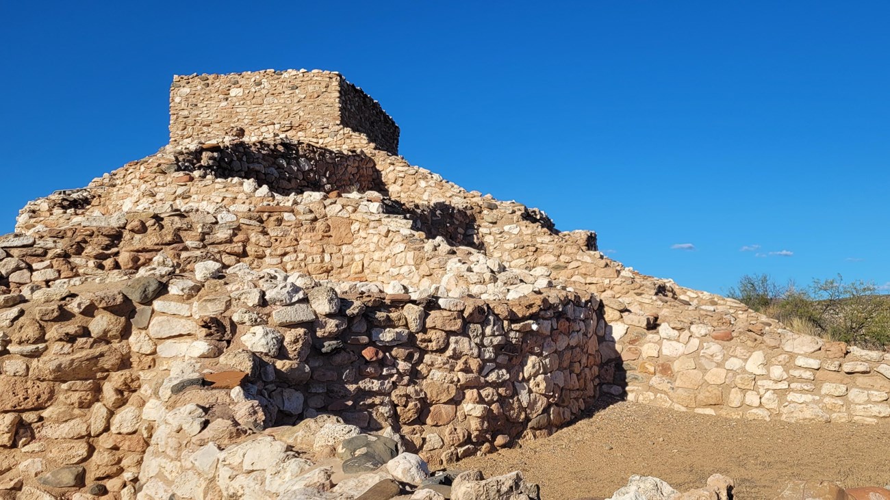 remains of a hilltop dwelling with walls creating square shaped rooms and a tall, central tower