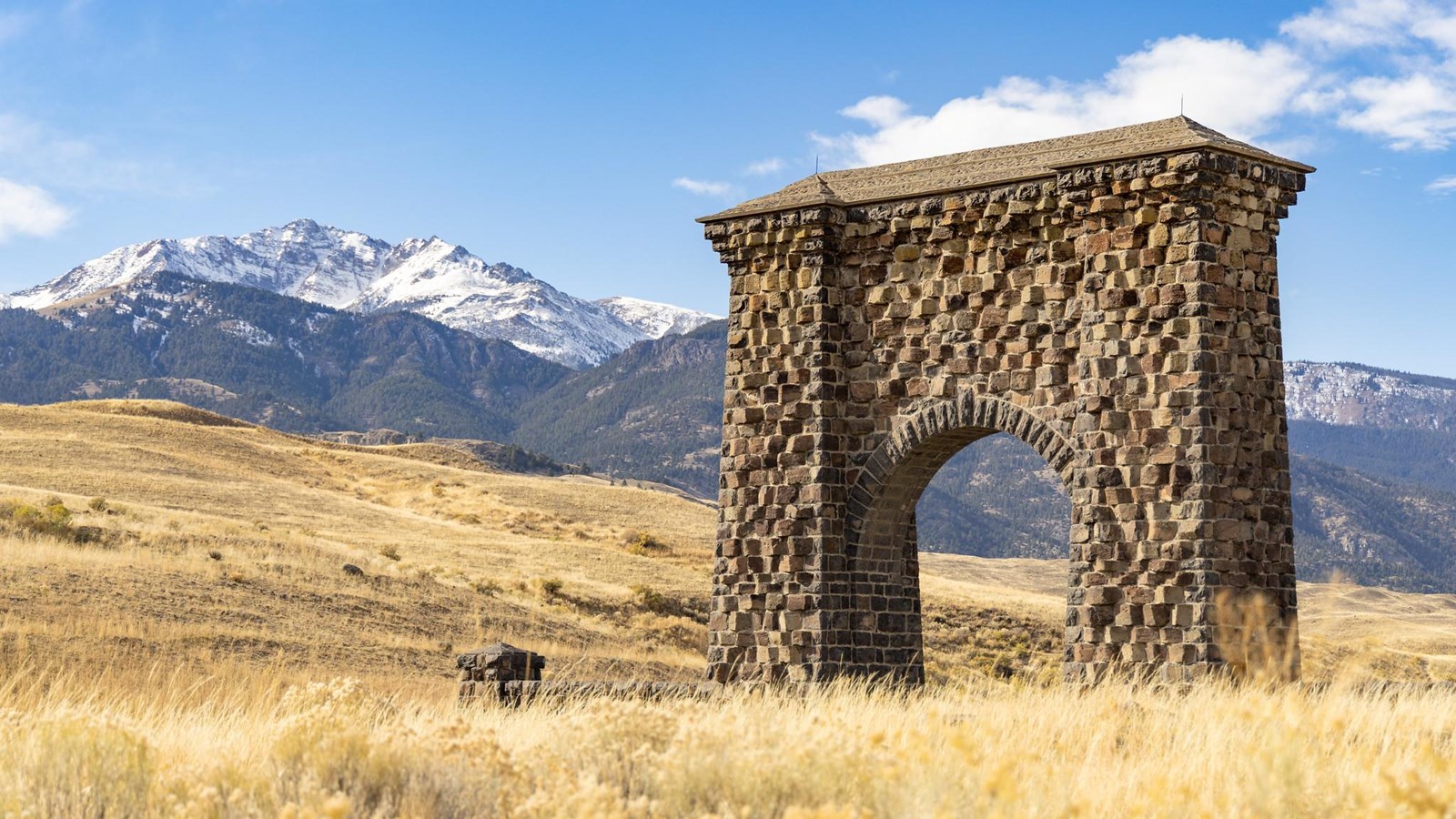 A grand, stone arch stands in front of snow-covered mountains.