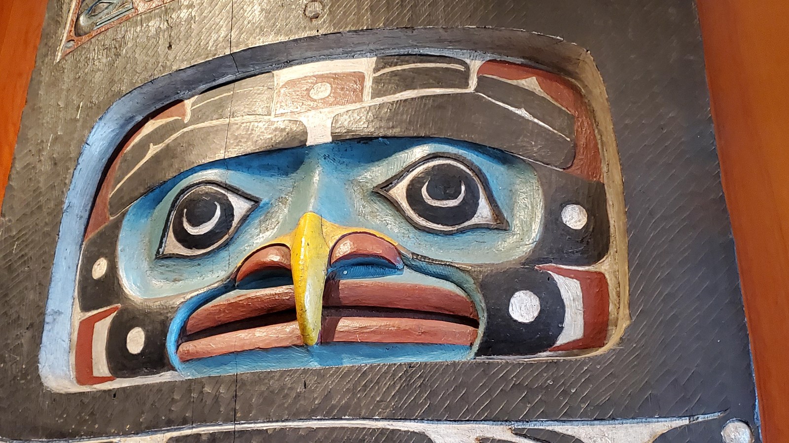 A portion of a carved and painted house post featuring a yellow beak in a formline eagle face