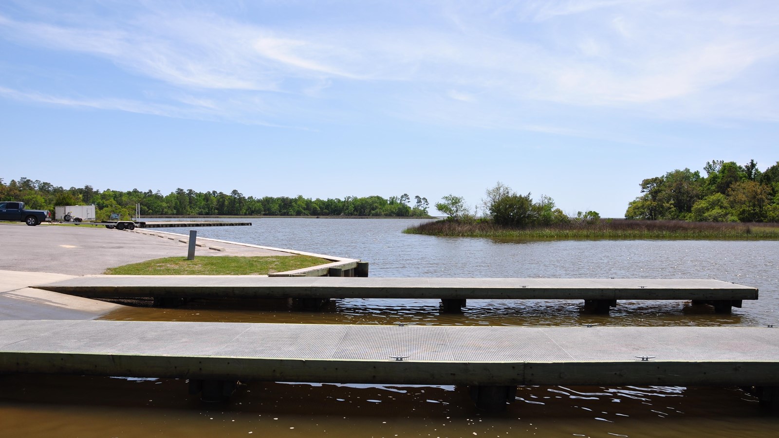Two wooden docks stand in front of a pavement ramp overlooking the bayou.