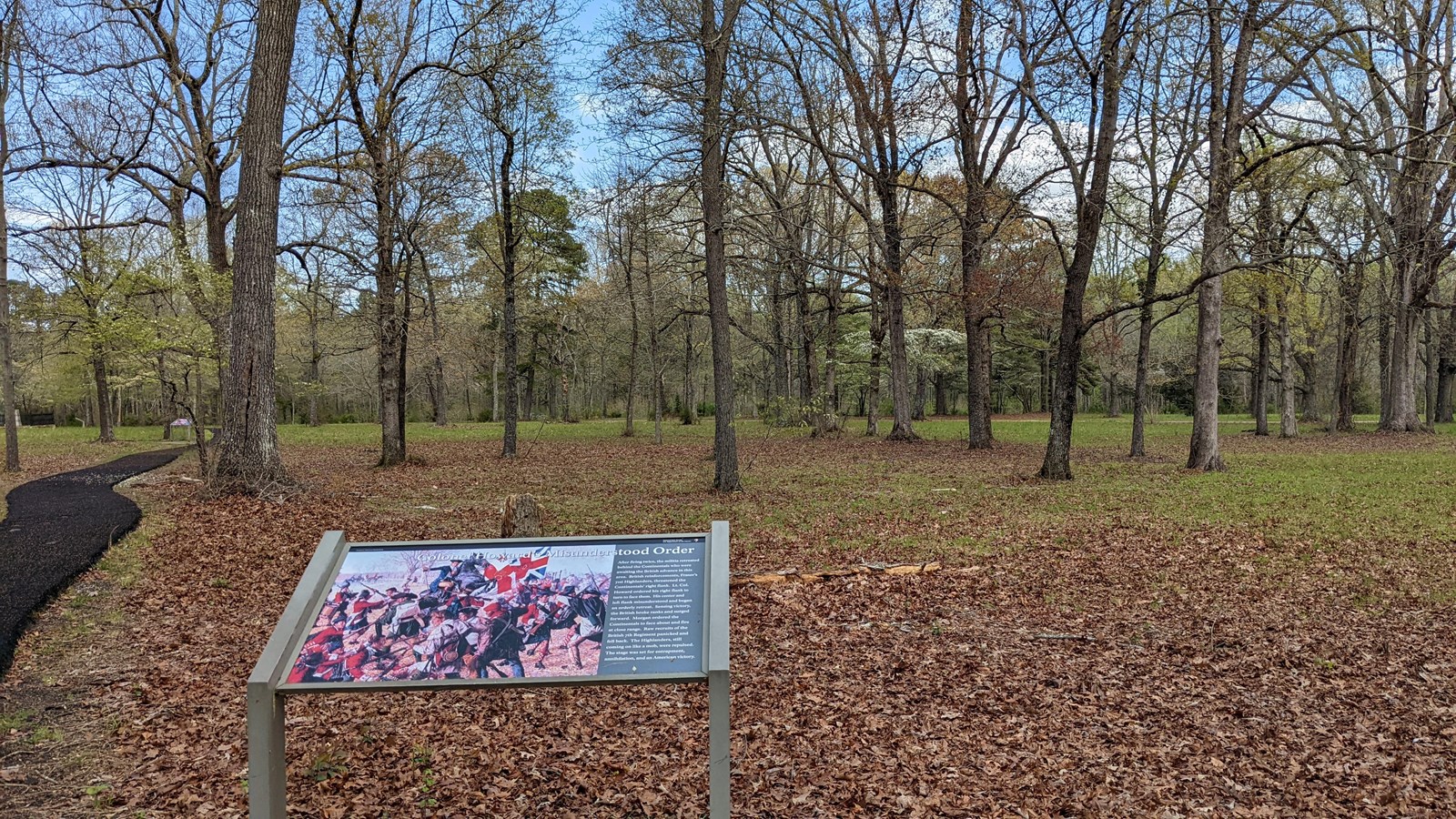 way side with a paved path on the left and trees in the background.