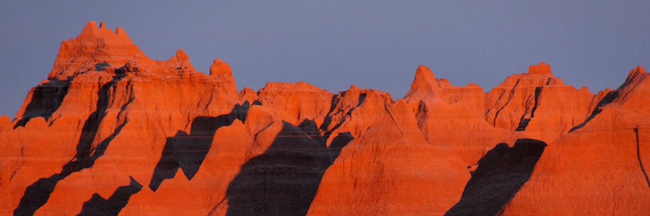 badlands buttes are illuminated by red sunlight, which creates shadows in the canyons.