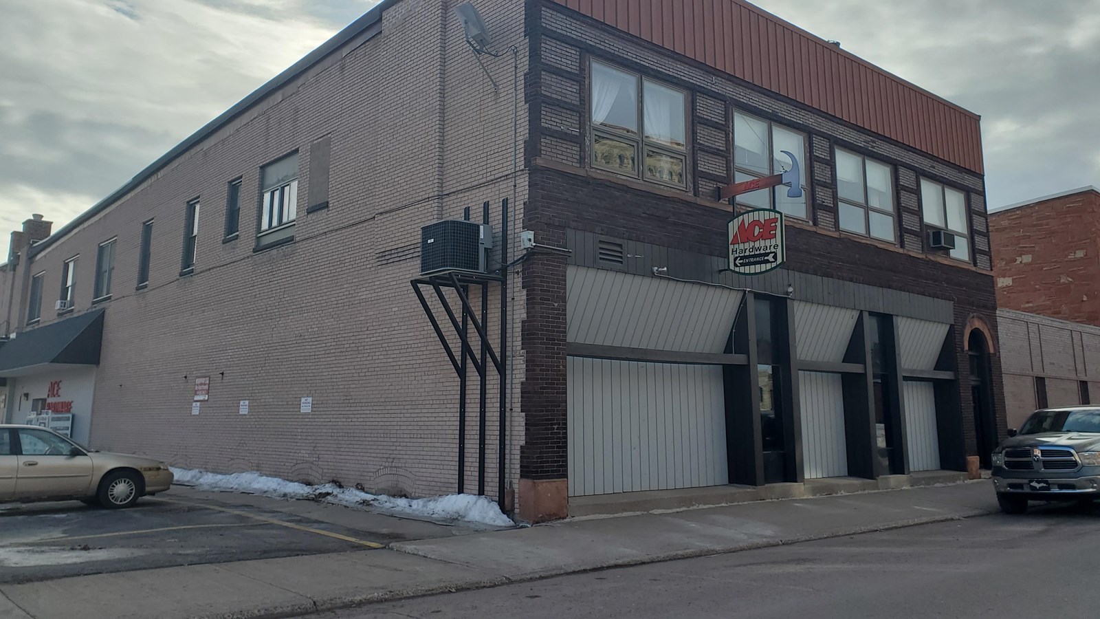 Two story red and yellow brick building with windows on the second story, a sign reads Ace Hardware.
