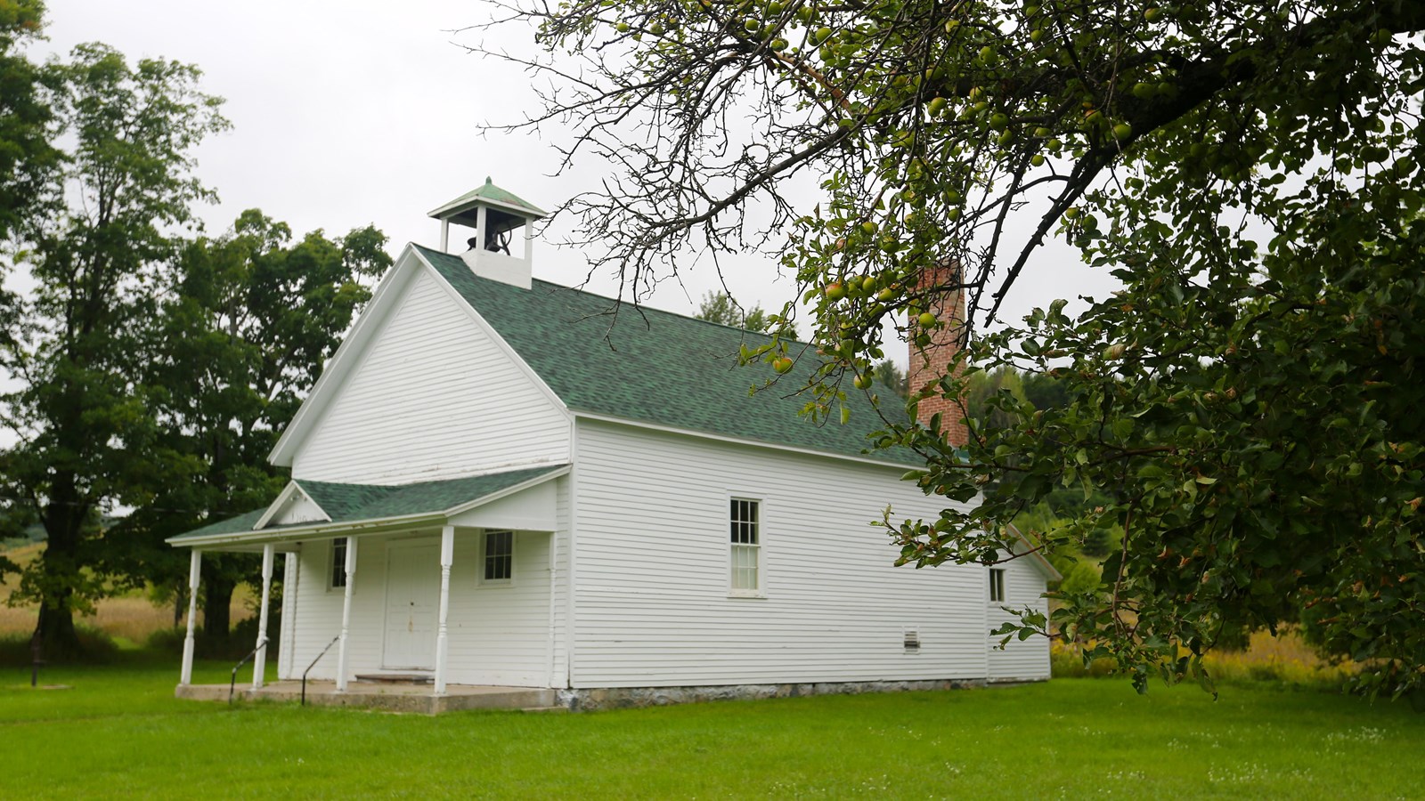 A small white building with front porch and bell in white small cupola on the roof