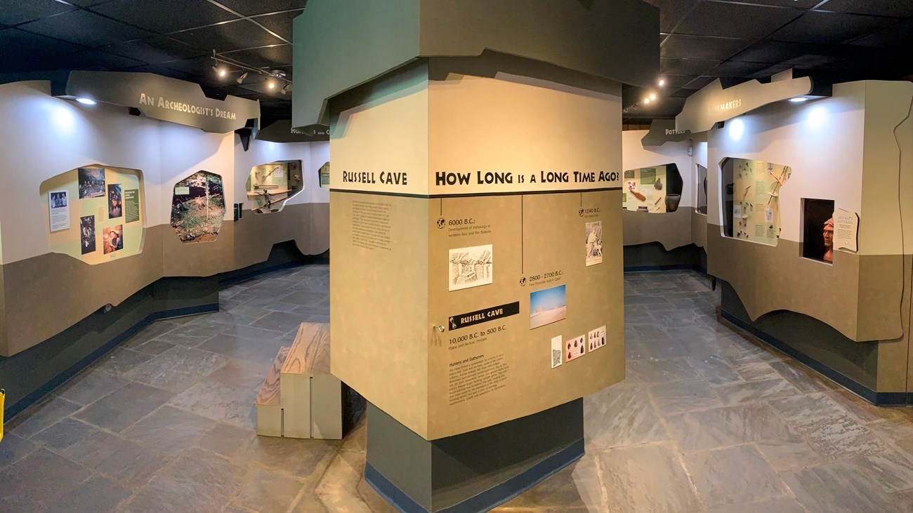 A large center pillar stands in a room surrounded by exhibit walls with glass cases showing artifact