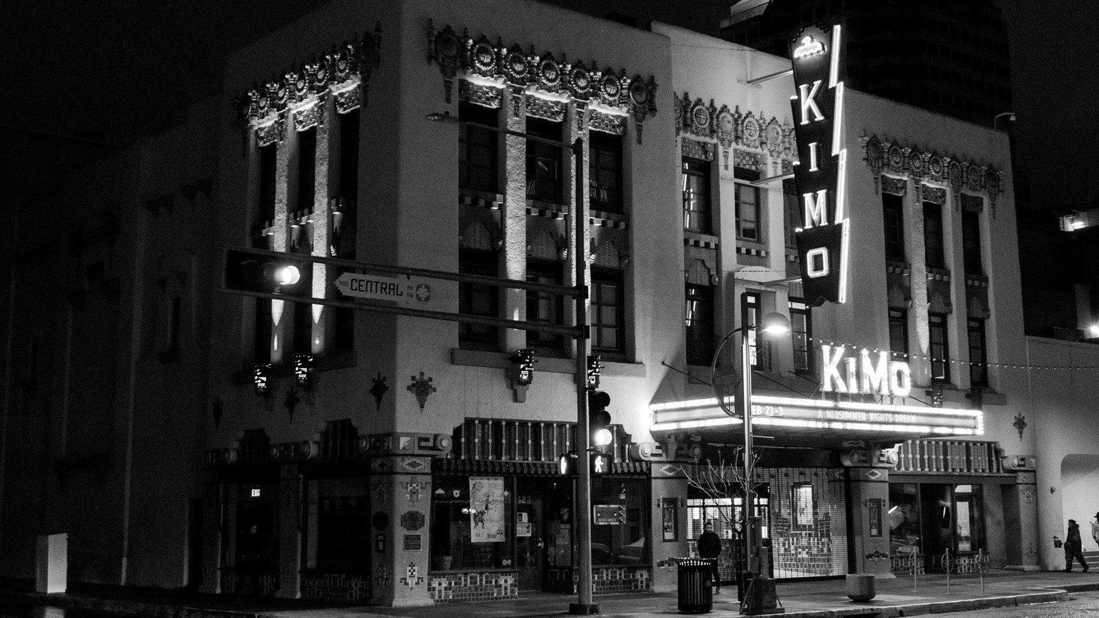 A black and white image of a three story stucco building with ornate detailing. A sign reads 