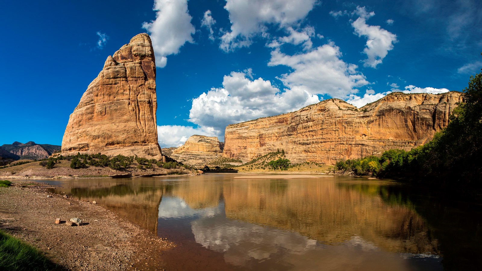 A large triangular sandstone rock in a canyon with a river flowing around it.
