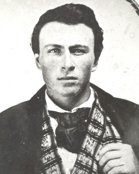 A young man wearing a coat, checkered vest, and tie.