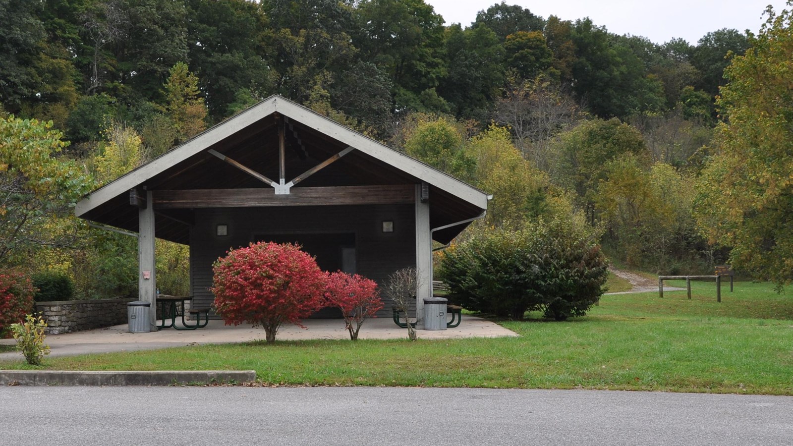 Picnic pavilion with tables underneath is center of picture. red colored bush is in front of tables