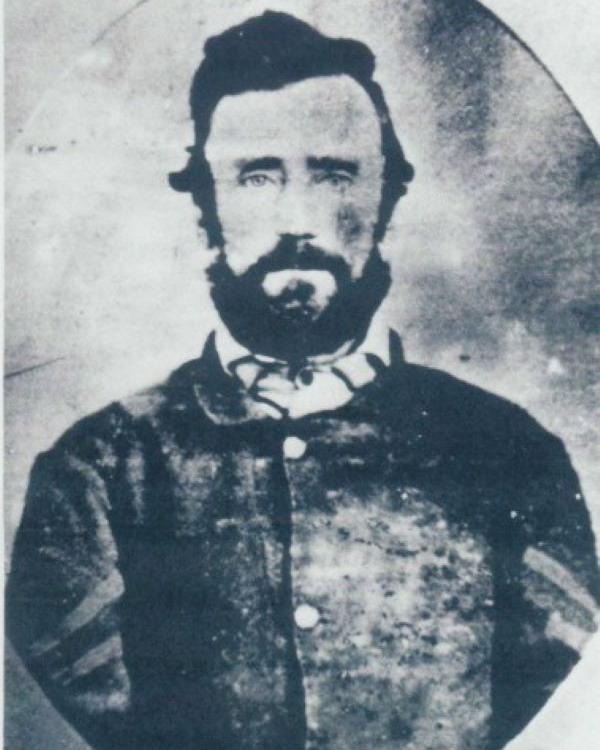 Young man with a full beard wearing a union civil war uniform with corporal stripes on his sleeves.