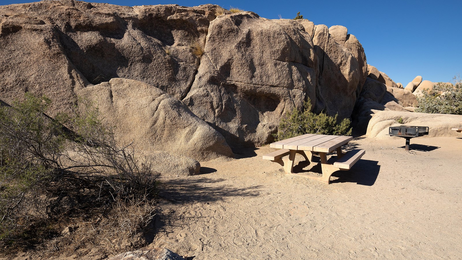 A picnic table and grill in front of a large rock formation.