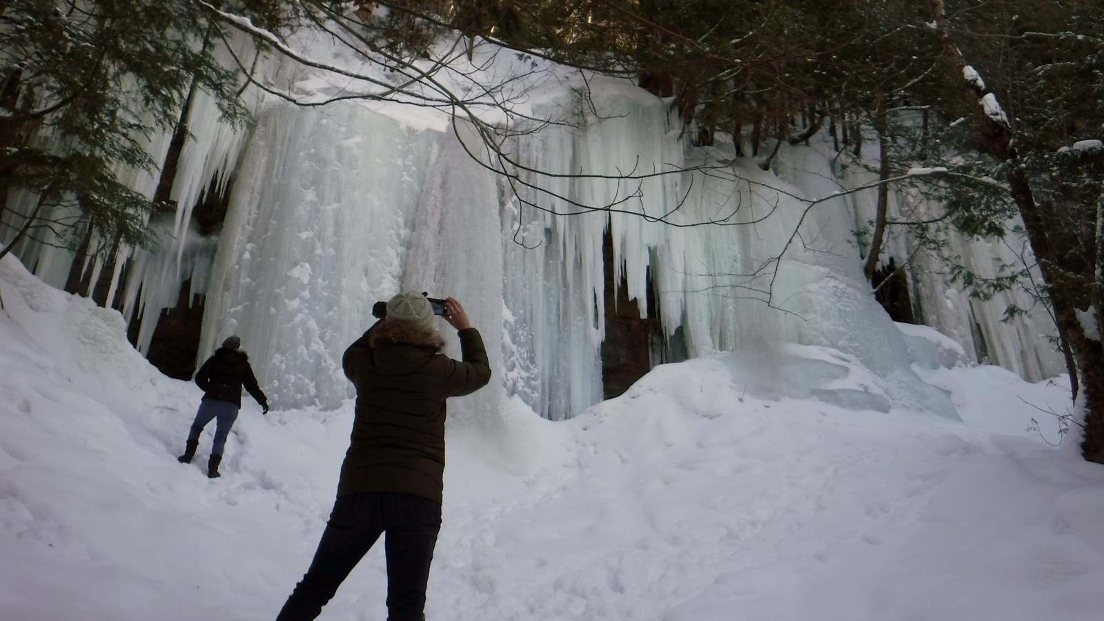 Visitor taking a picture of ice curtains hanging from 20 ft cliff.