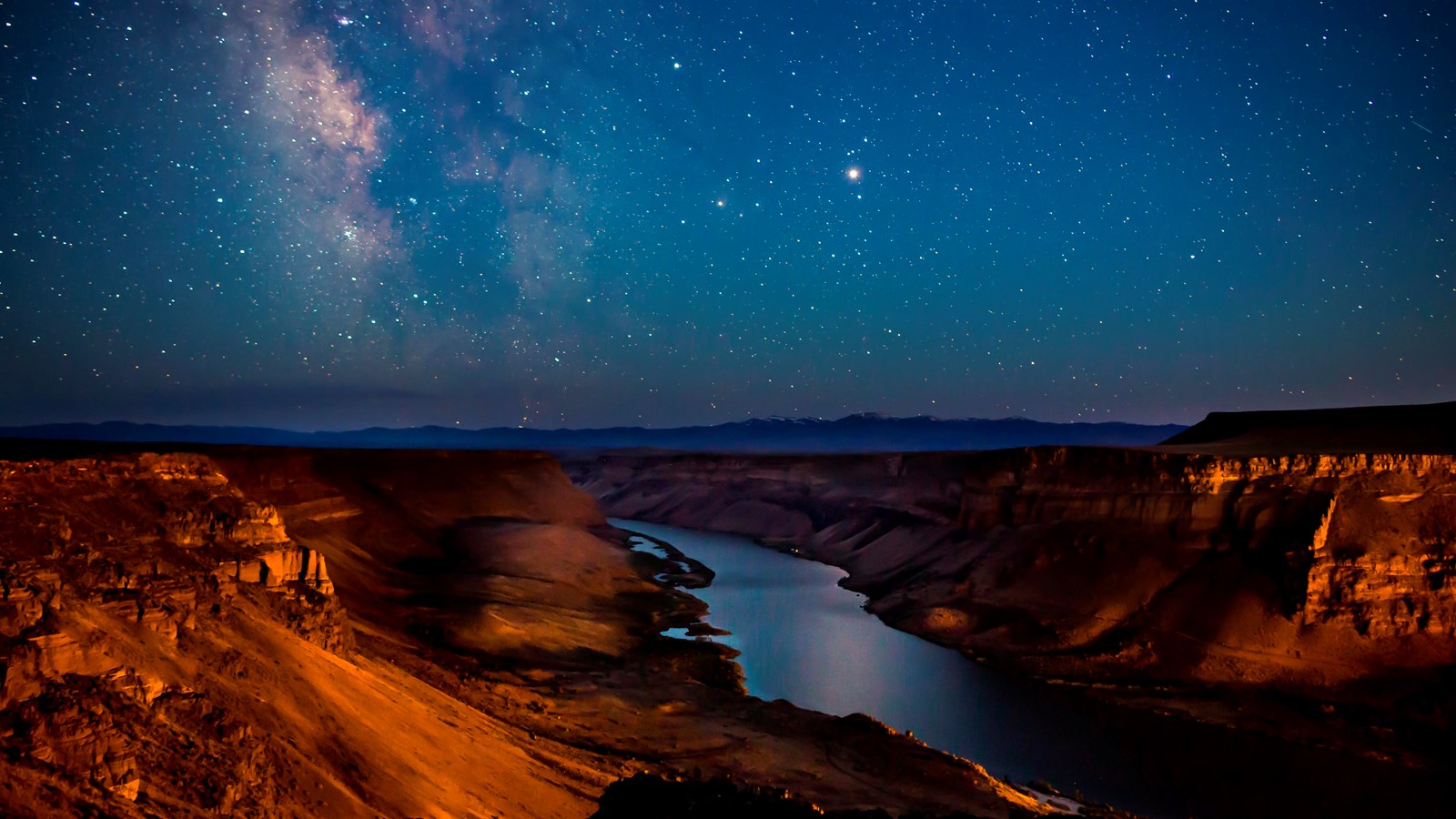 Photograph of Snake River at night, with stars visible above. The river is going through steep canyo
