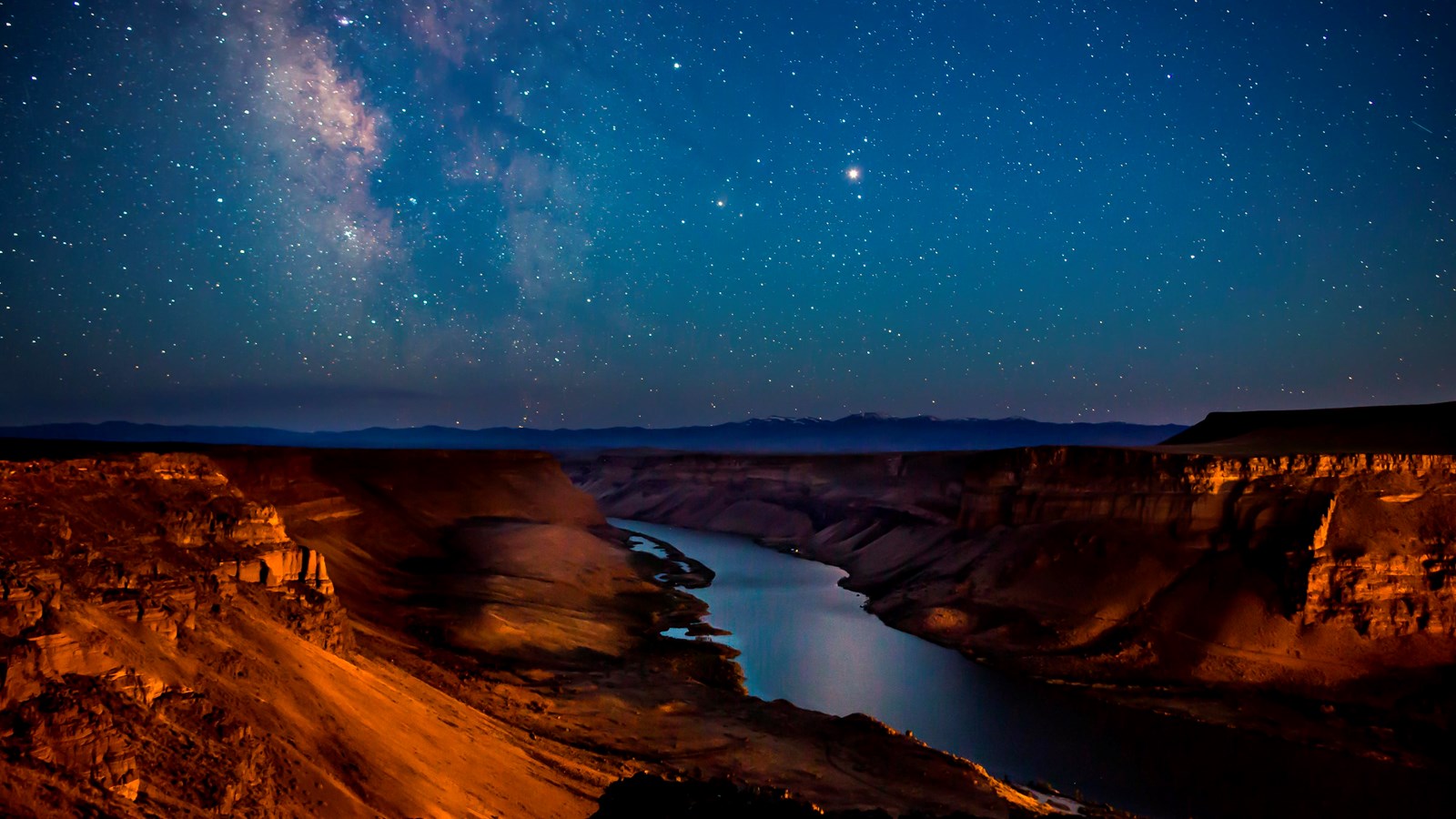 Photograph of Snake River at night, with stars visible above. The river is going through steep canyo