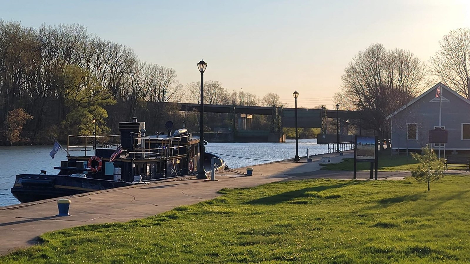 A small tug boat is tied up along a river-side walkway.