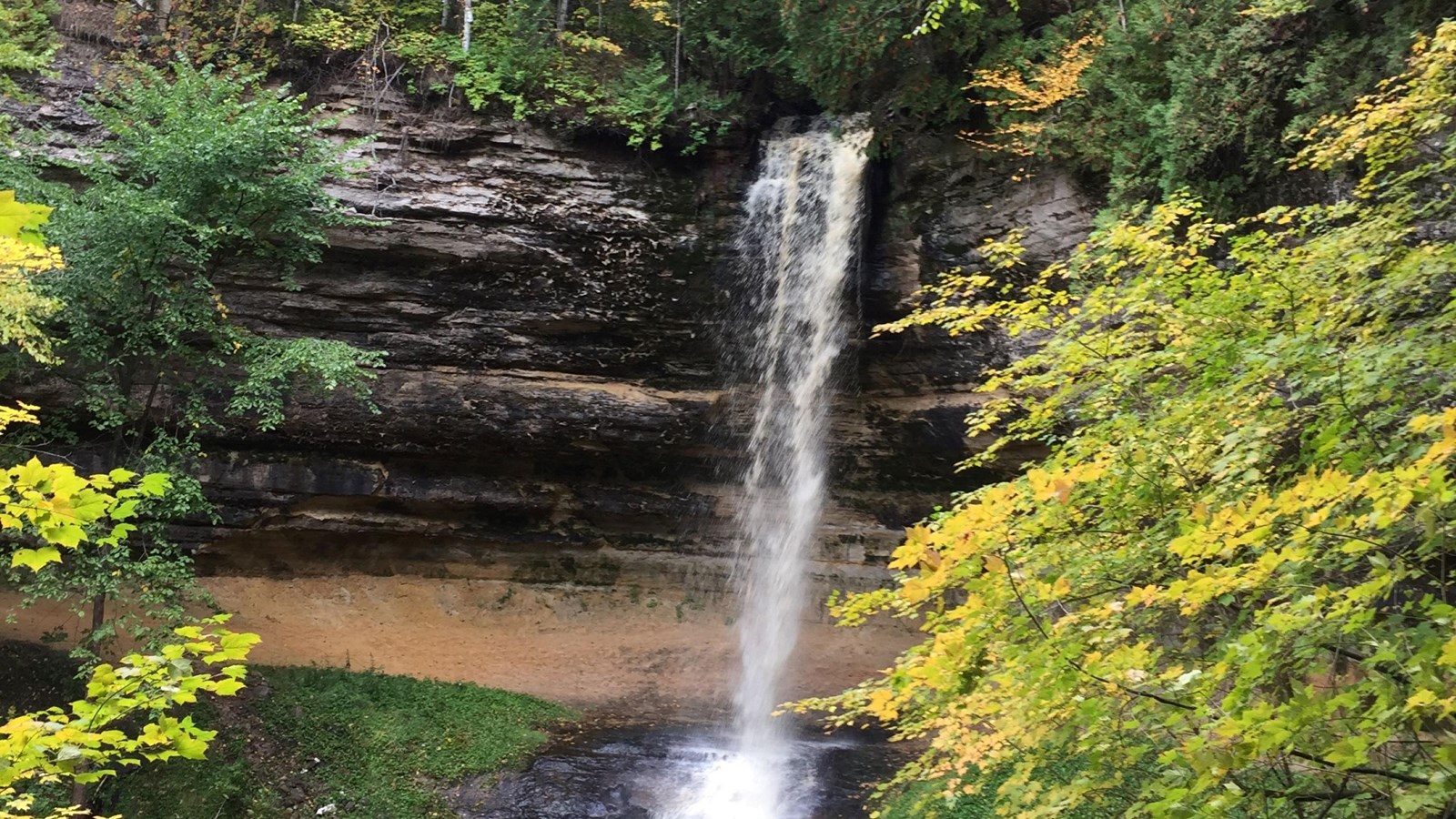 Munising Falls flows 50 feet over the sandstone rock ledge. Yellow and green leaves on the trees in 