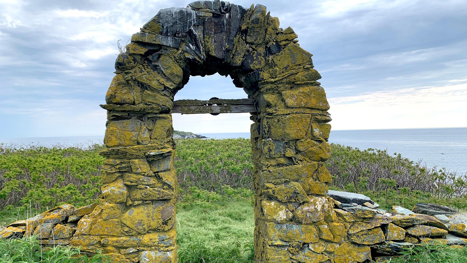 stone archway still present on the island. Both greenery and the water is seen in the background.