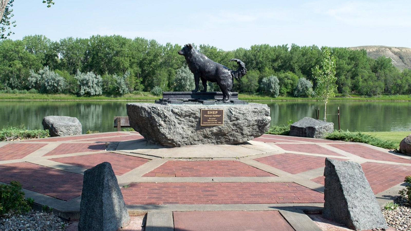 A bronze statue of a dog atop a granite block surrounded by a brick plaza