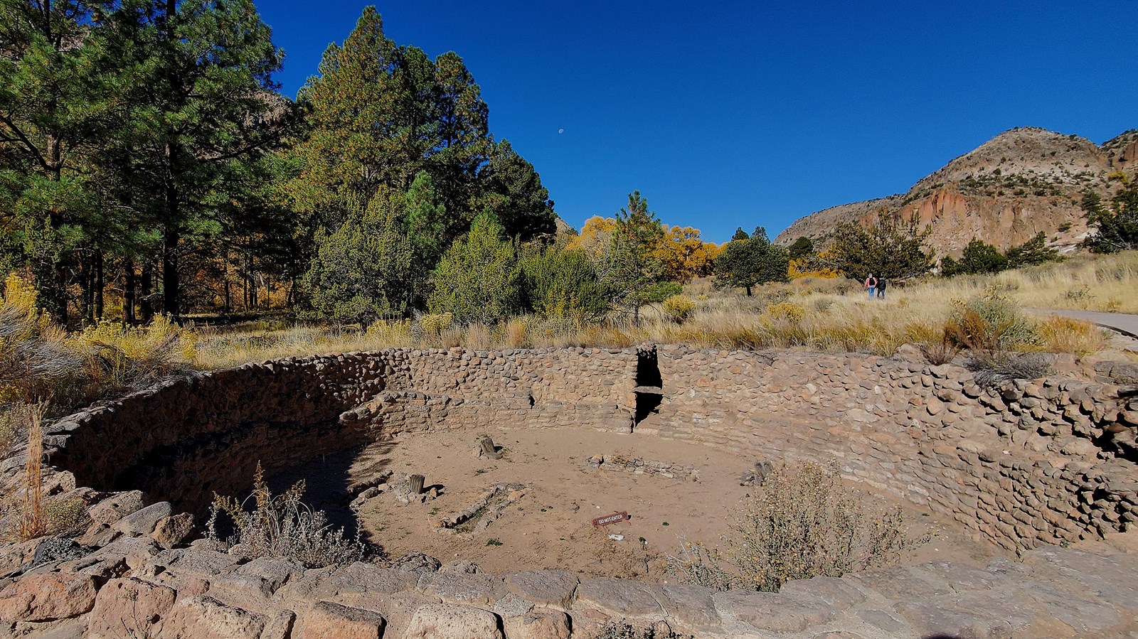 a stone lined depression in the ground with green trees and blue sky