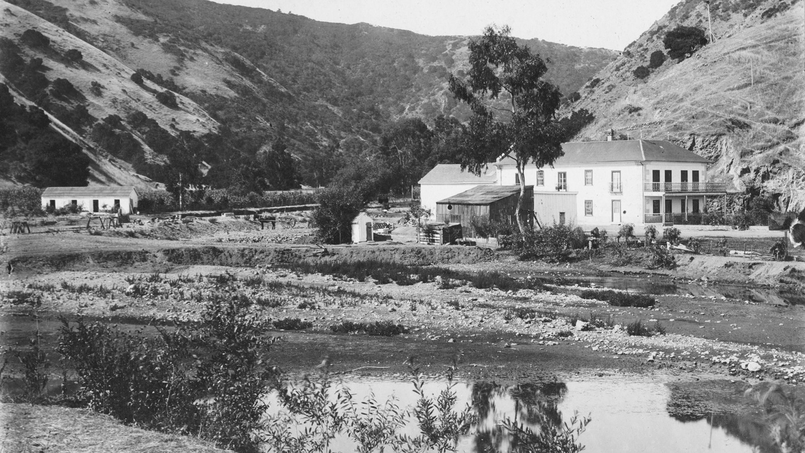 Two story ranch house with 3 other buildings nearby with a wetland in the foreground.
