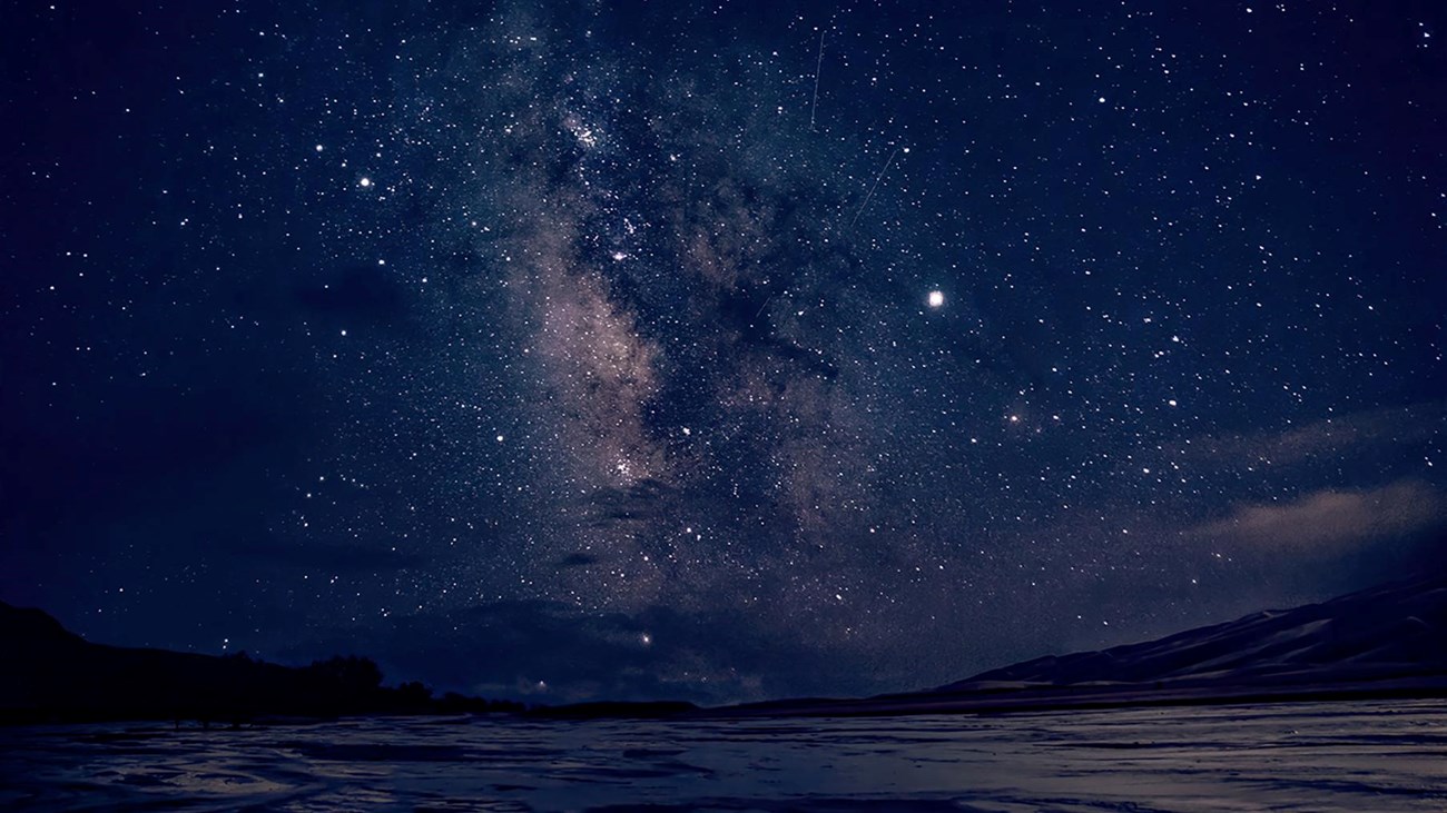 The Milky Way over a shallow stream flowing across sand at night