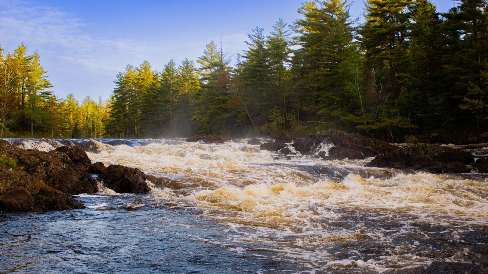 A fast-flowing river drops down a small waterfall with rocks and trees on either side.