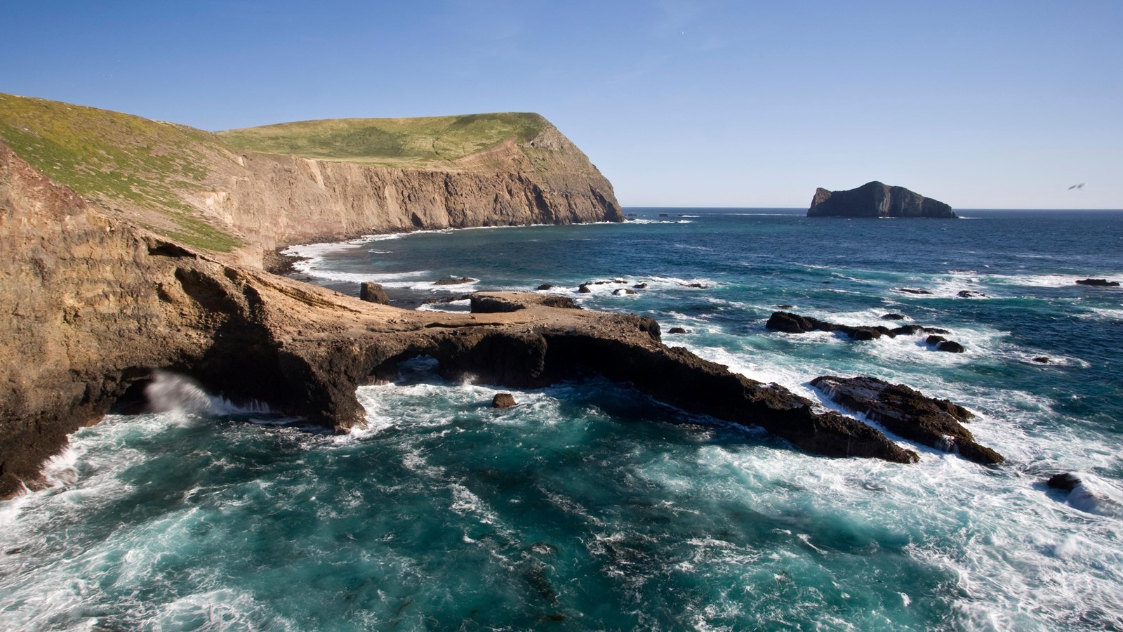 rocky coast with arch in foreground and islet in background.