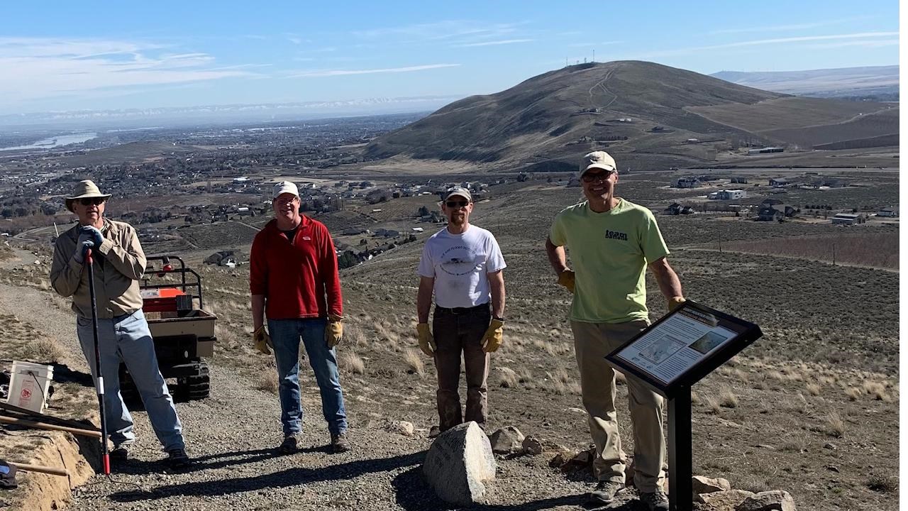 Color photograph of a group of 4 people on a hiking trail ascending a mountain.