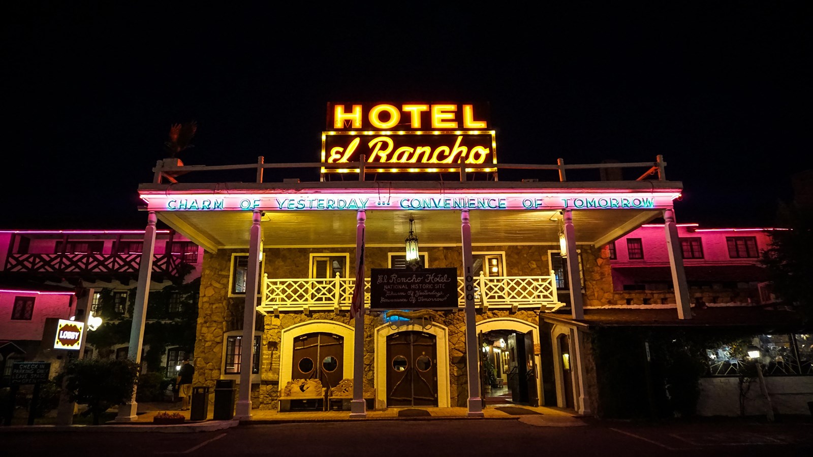 A two story building at night with pink and yellow neon lights. A sign reads 