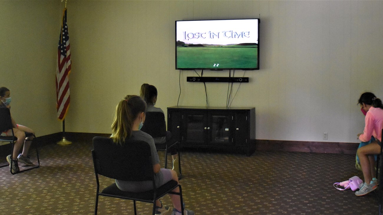 Several children sit watching the video play on a tv screen