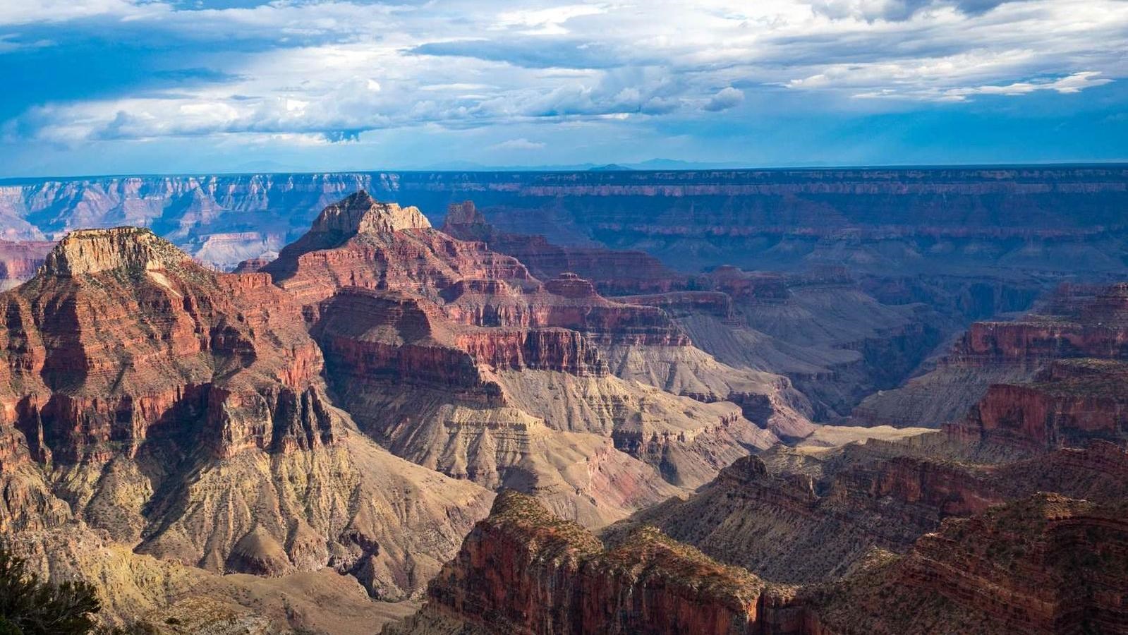 A partly cloudy sky casts shadows on the canyon landscape while sunlight highlights nearby cliffs.