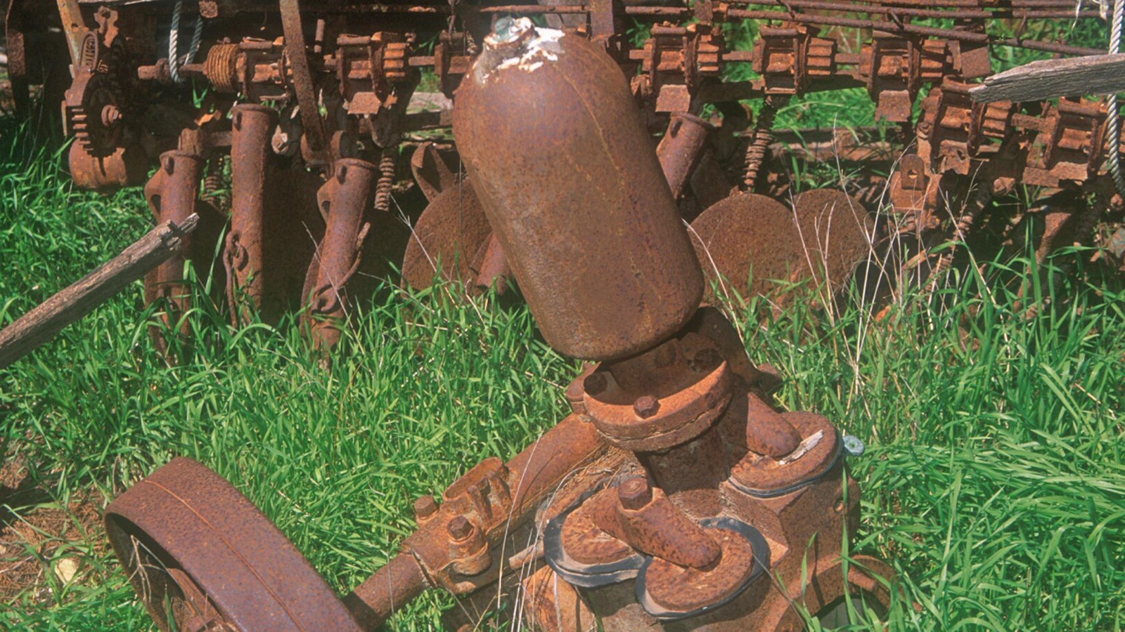 This rusted water pump has a large wheel and a cylinder on top. No other information is available.