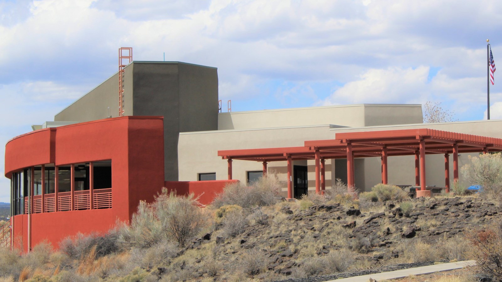 A tan, red, and black building sits under a slightly cloudy sky.