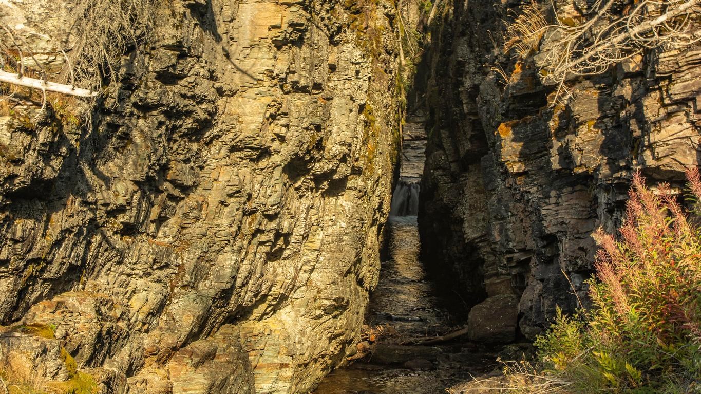 Light fills a narrow canyon as water streams through the crack in the rocks.