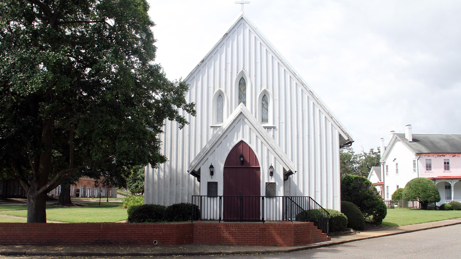 A wood board-and-batten sided chapel building has Gothic Revival features and is painted white.