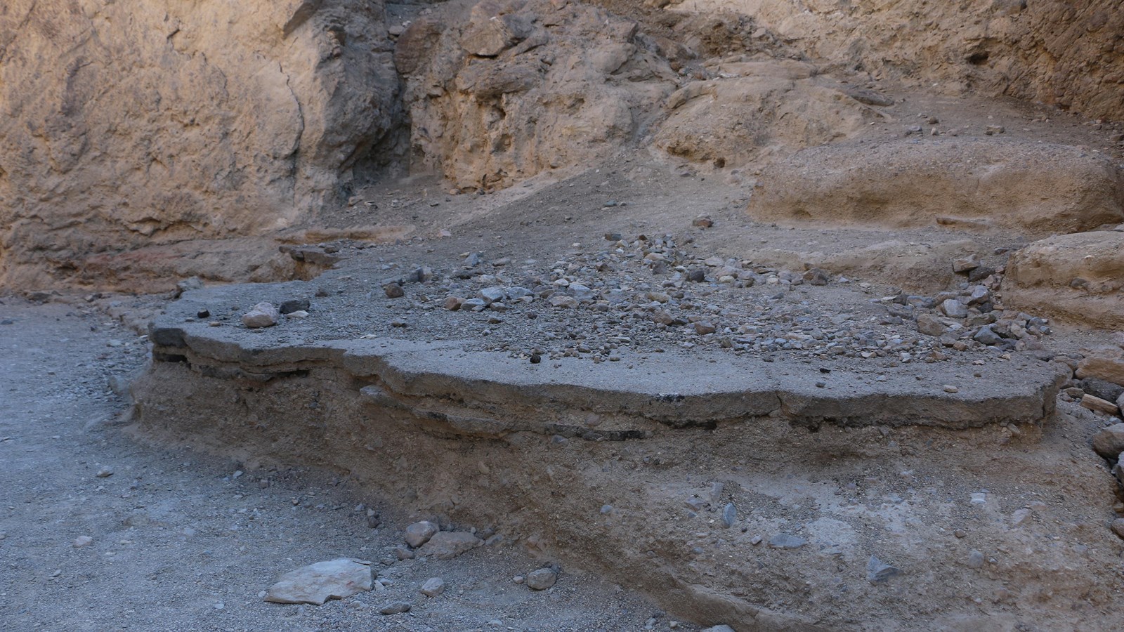 A knee-high slab of pavement rests on a rock slab while tan canyon walls tower behind.